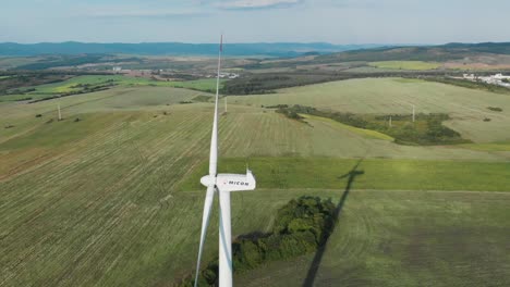 Aerial-arc-shot-around-single-wind-turbine-generator-in-grass-field