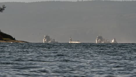 In-the-distance,-a-small-Naval-convoy-travels-Puget-Sound,-the-ships-and-submarine-are-illuminated-by-the-sun