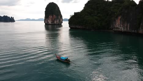 Drone-footage-of-longtail-boat-navigating-around-islands-of-Thailand-with-the-limestone-rock-formations-sticking-out-of-the-water-and-the-ocean-in-background-4