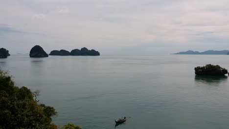 Drone-footage-of-longtail-boat-navigating-around-islands-of-Thailand-with-the-limestone-rock-formations-sticking-out-of-the-water-and-the-ocean-in-background