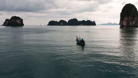 Drone-footage-of-longtail-boat-navigating-around-islands-of-Thailand-with-the-limestone-rock-formations-sticking-out-of-the-water-and-the-ocean-in-background-6