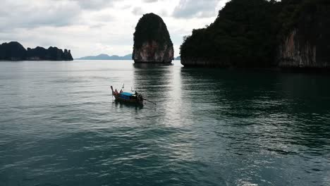 Drone-footage-of-longtail-boat-navigating-around-islands-of-Thailand-with-the-limestone-rock-formations-sticking-out-of-the-water-and-the-ocean-in-background-5