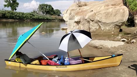 Guy-relaxing-under-umbrella-in-canoe-on-river-banks-in-Utah