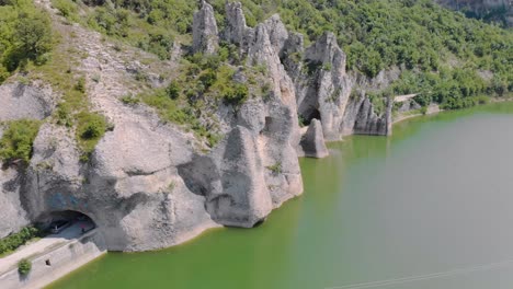 Panoramic-aerial-footage-of-beautiful-cliffs-with-road-tunnels-surrounded-by-lake