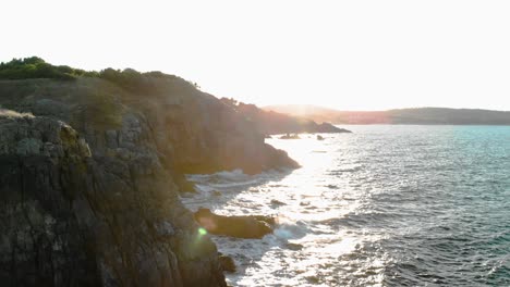 Aerial-pan-shot-of-sun-rays-illuminate-through-big-seashore-cliffs-in-sunset,-Bulgaria