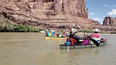 Guys-paddling-canoes-down-river-near-sandstone-cliffs-in-Utah