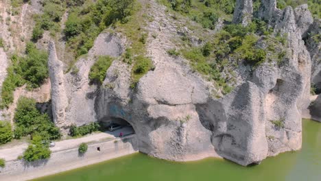 Aerial-arc-footage-of-beautiful-cliffs-with-road-tunnel-surrounded-by-lake