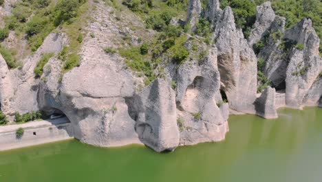 Panning-aerial-footage-of-beautiful-cliffs-with-road-tunnels-surrounded-by-lake