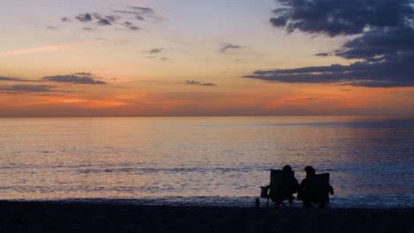 Paar-Sitzt-Auf-Stühlen-Am-Strand-Und-Beobachtet-Den-Sonnenuntergang