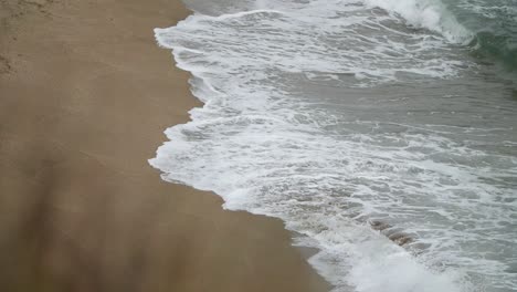 Side-view-of-waves-deepening-the-sand,-shot-in-slow-motion-with-tele-lens-from-a-higher-point-of-view