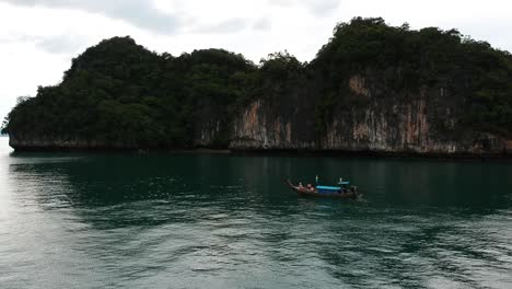 Drone-footage-of-longtail-boat-navigating-around-islands-of-Krabi,-Thailand-with-the-limestone-rock-formations-sticking-out-of-the-water-and-the-ocean-in-background