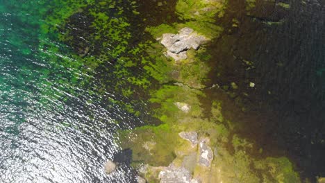 Vertical-aerial-shot-of-rocky-sea-cost-in-sunny-summer-day