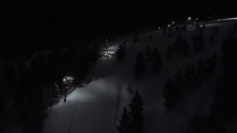 Aerial-of-snow-machine-at-work-in-Idre,-Sweden-during-a-late-evening-in-the-dark