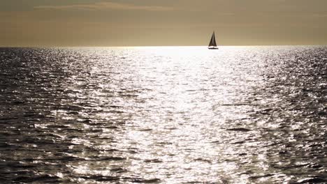 Slow-motion-shot-of-sailboat-silhouette-passing-through-sun-reflection-on-water