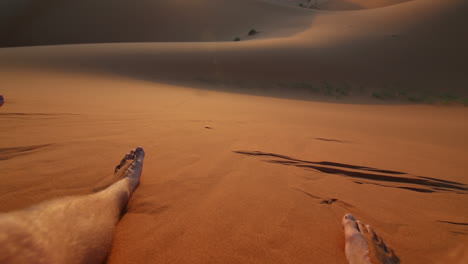 Tilt-up-shot-towards-the-sunset-with-a-backpacker-hanging-his-feet-in-the-dunes