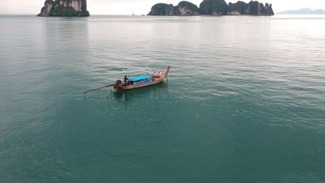 Drone-footage-of-longtail-boat-navigating-around-islands-of-Thailand-with-the-limestone-rock-formations-sticking-out-of-the-water-and-the-ocean-in-background-9