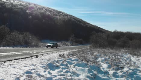 Wide-full-shot-of-a-car-drive-in-winter-day-on-dry-road-and-snowy-background