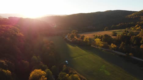 Aerial-epic-drone-shot-of-sun-rays-in-grass-field-surrounded-by-forest-at-sunset-4