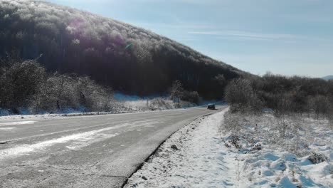 Wide-full-shot-of-a-car-pass-and-disappear-in-winter-day,-dry-road-and-snowy-background