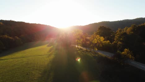 Aerial-epic-drone-shot-of-sun-rays-in-grass-field-surrounded-by-forest-at-sunset-2
