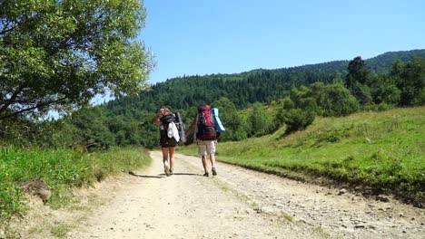 Couple-with-backpacks-walking-on-th-eroad-at-the-mountains