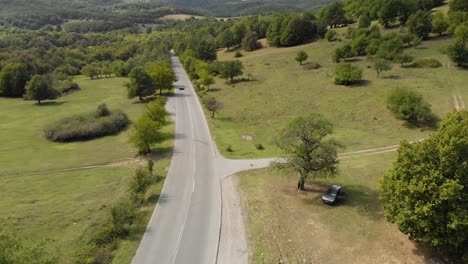 Aerial-drone-shot-over-extra-urban-road-in-valley-and-car-pass-uphill