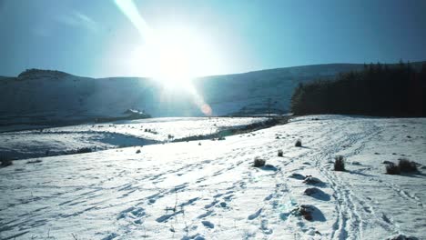 Pan-across-snow-covered,-English-mountain-side-with-natural-lens-flare-from-the-winter-sun