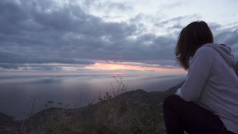 Girl-squat-on-a-high-cliff-and-watch-the-sunset-through-cloudy-sky-over-Adriatic-sea-1