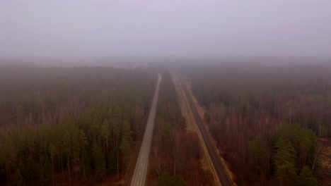 Drone-footage-of-forest,-road-and-railway-during-cloudy-day-in-rural-landscape