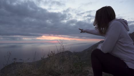 Girl-squat-on-a-high-cliff-and-watch-the-sunset-through-cloudy-sky-over-Adriatic-sea-2