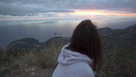 Girl-squat-on-a-high-cliff-and-watch-the-sunset-through-cloudy-sky-over-Adriatic-sea