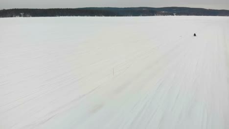Toma-Aérea-De-Seguimiento-De-Un-Hombre-Conduciendo-Su-Moto-De-Nieve-En-Indalsalven-En-Timra,-Sundsvall,-Suecia