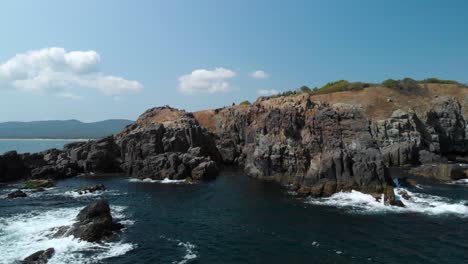 Aerial-pan-shot-of-big-rocks-in-the-sea-next-to-the-shore-in-sunny-summer-day