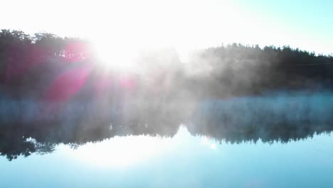 Sunrise-over-forest-in-front-of-foggy-lake---panning-shot