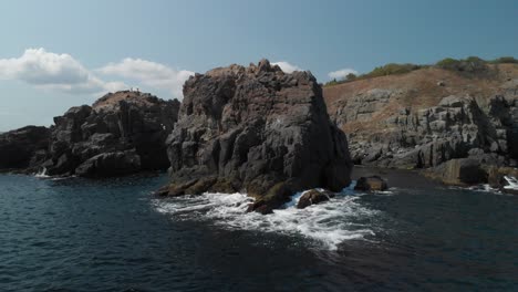 Aerial-pan-shot-around-big-rocks-in-the-sea,-sunny-summer-day