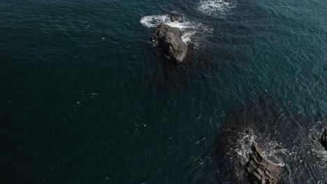 Aerial-shot-over-rocks-in-the-sea,-sunny-summer-day