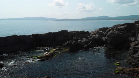 Aerial-pan-shot-around-big-rocks-in-the-sea-next-to-the-shore-in-sunny-summer-day-2