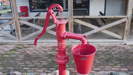 Eine-Alte-Rote-Wasserpumpe-Mit-Einem-Daran-Hängenden-Eimer