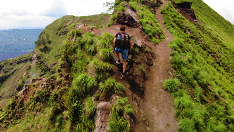 Drone-following-an-European-tourist-wearing-a-backpack,-walking-to-the-top-of-an-active-vulcano-Mount-Batur-in-Bali,-Indonesia