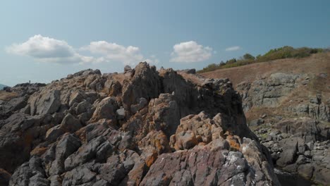 Aerial-tracking-shot-over-big-rocks-on-the-seashore-in-sunny-summer-day