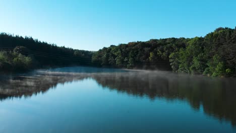 Foggy-lake-and-forest-after-sunrise---panning-shot-over-water