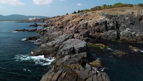 Aerial-pn-shot-around-big-rocks-in-the-sea-next-to-the-shore-in-sunny-summer-day