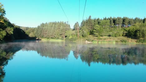 Early-morning-low-drone-shot-over-glossy-lake-under-wires