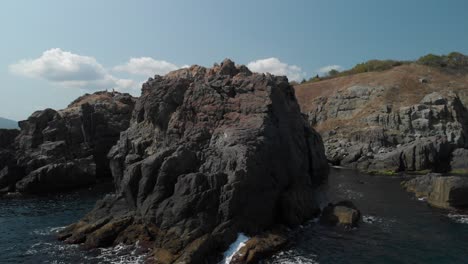 Aerial-tracking-shot-of-big-rocks-on-the-seashore-in-sunny-summer-day