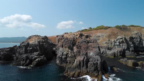 Aerial-tracking-shot-of-big-rocks-in-the-sea-from-the-seashore-in-sunny-summer-day
