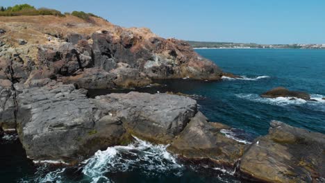 Aerial-pan-shot-around-big-rocks-in-the-sea-and-seagulls-in-sunny-summer-day