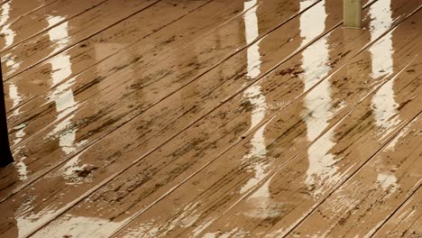 Rain-falling-on-a-water-damage-light-brown-tan-painted-deck,-with-some-reflection