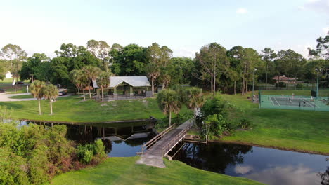 Pull-away-from-Lakeside-Park-with-Bridge,-Tennis-Courts-and-Gazebo