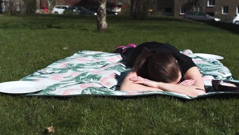 Woman-laying-on-a-blanket-in-the-sun-after-a-hard-workout,-totally-exhausted