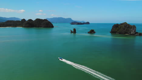 Drone-tracking-a-tour-boat-sailing-near-small-cliff-islands-of-Langkawi,-slow-motion-footage